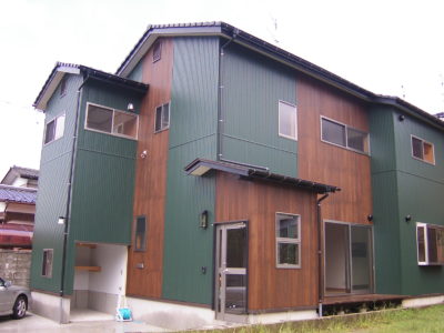 便利な屋外収納が付いた木目と緑の外壁がおしゃれな二世帯住宅